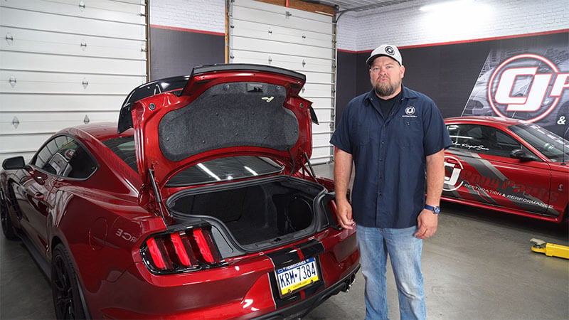 Mechanic standing in front of a S550 Mustang with the trunk open