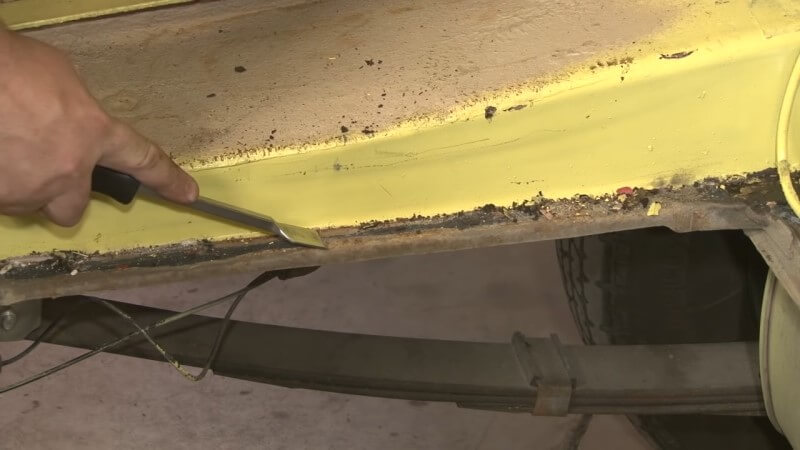 Mechanic scraping off the old sealant with a scraper