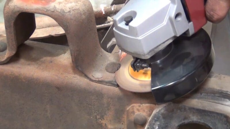 A mechanic using an angle grinder to cut the heads off of the factory rivets on the frame
