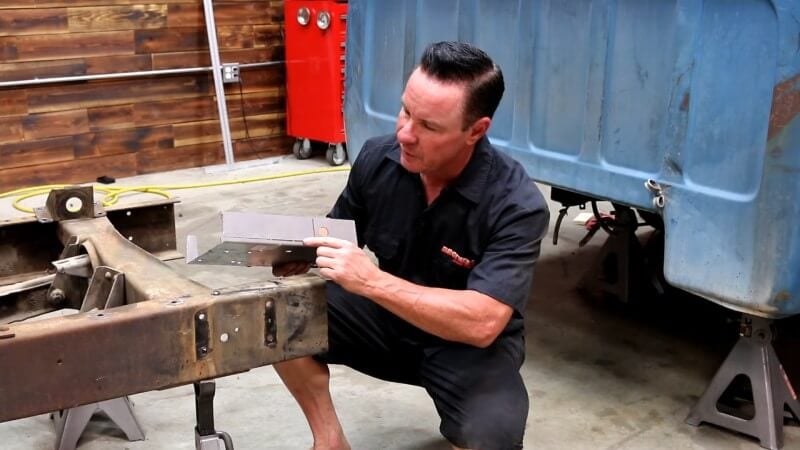 A mechanic kneeling in front of the disassembled truck and pointing at the section of the conversion template that needs to be cut