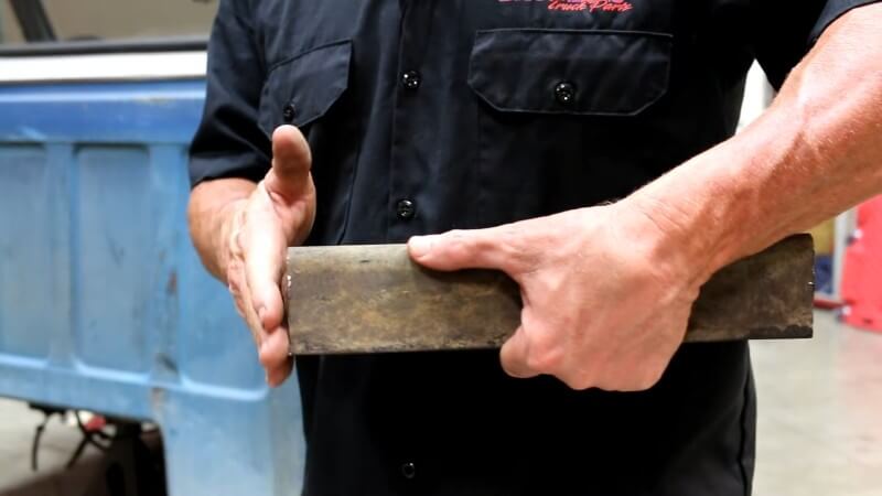 A close up of a mechanic showing the camera a properly squared off piece of old frame