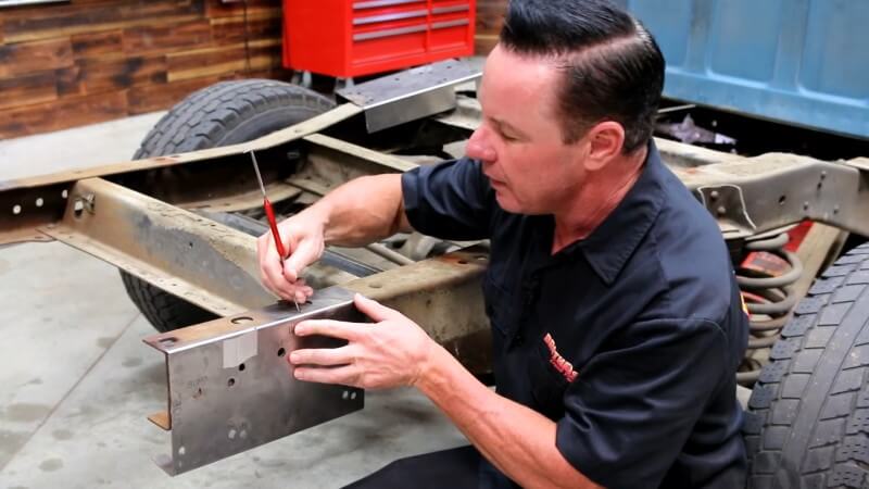 A mechanic using kneeling in front of the rear frame section and marking a cut line on the modified template