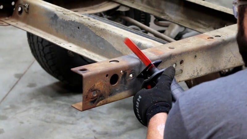 A mechanic using a sawzall to cut off excess frame material on the rear frame section