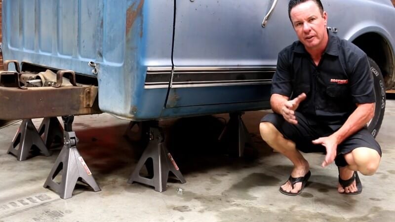 A wide angle shot of a mechanic sitting in front of a fully suspended truck with multiple jack stands underneath it