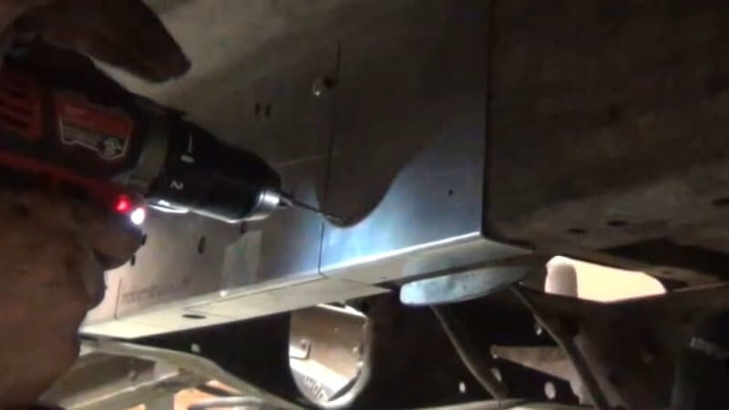 A mechanic using a drill to drill out the necessary pilot holes into the frame as directed by the template