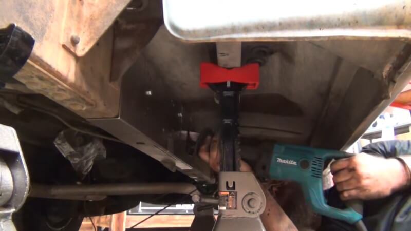 A mechanic using a sawzall to cut the frame of the classic Chevy truck