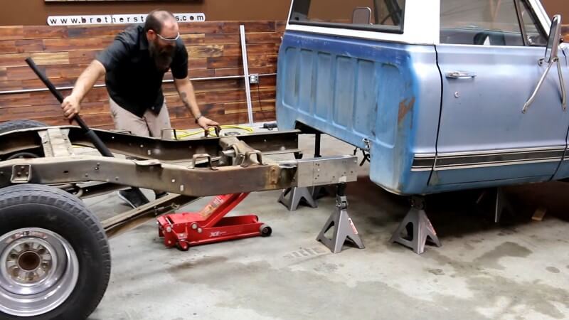 A mechanic carefully moving the rear frame section out from underneath the truck with a red hydraulic floor jack
