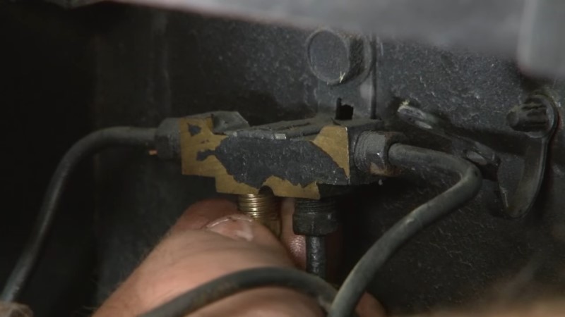 A mechanic screwing in a plug into the distribution block after removing the rear brake line