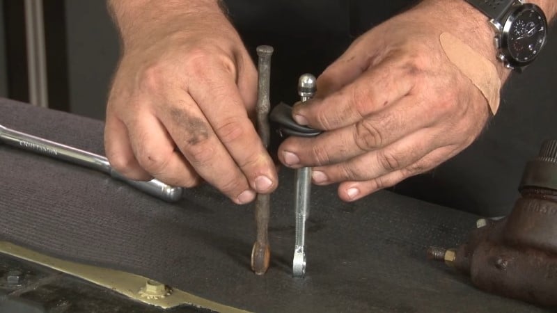 Mechanic comparing the length of the factory pushrod and the replacement pushrod
