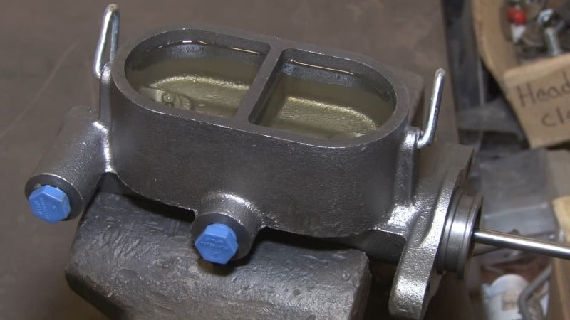 Mechanic bleeding the replacement master cylinder with a flathead screwdriver