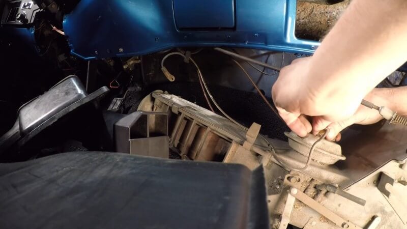 A mechanic using his hands to carefully disconnect the vacuum hoses from the heater box