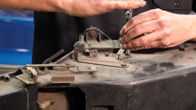 A close up of a mechanic using a screwdriver to remove the heater box cover on the side of the assembly