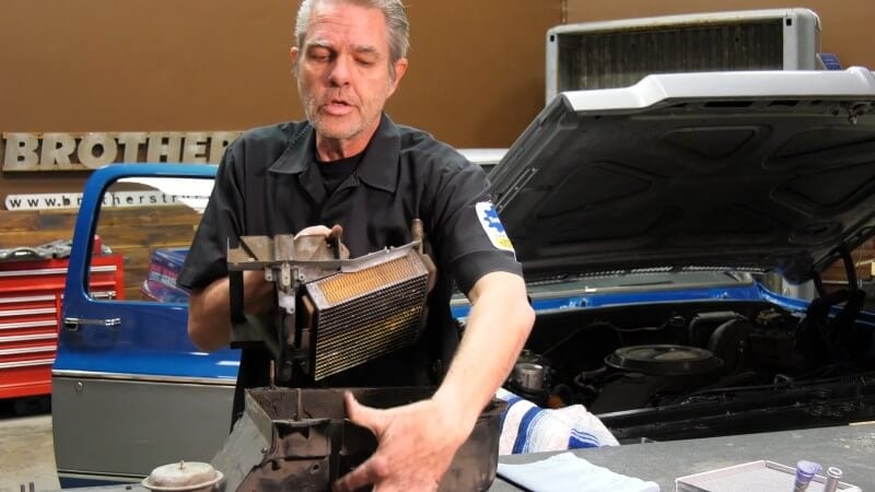 A mechanic standing in front of a table removing the heater core assembly from the top of the heater core box