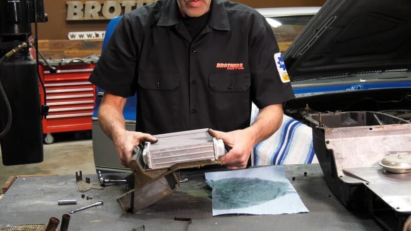 A mechanic standing in front of a table holding the heater core assembly and sliding the new heater core into place on the assembly