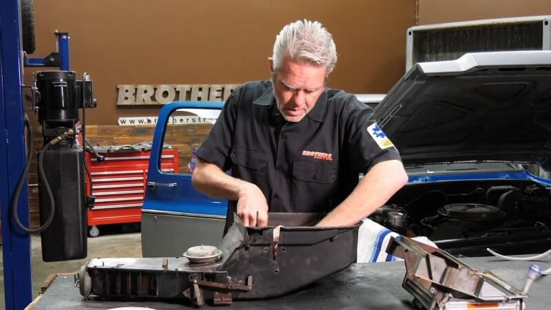 A mechanic standing in front of a table holding the heater core assembly and inserting the new gasket into place inside the assembly