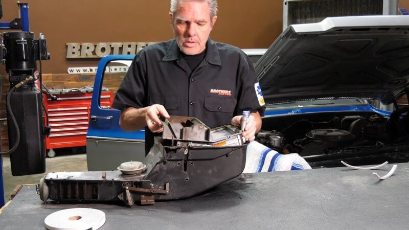 A mechanic standing in front of a table holding the heater core assembly and sliding the heater core assembly back into the heater core box