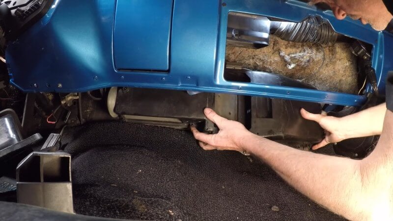 A close up of a mechanic gently pushing the heater box into place against the firewall underneath the dashboard