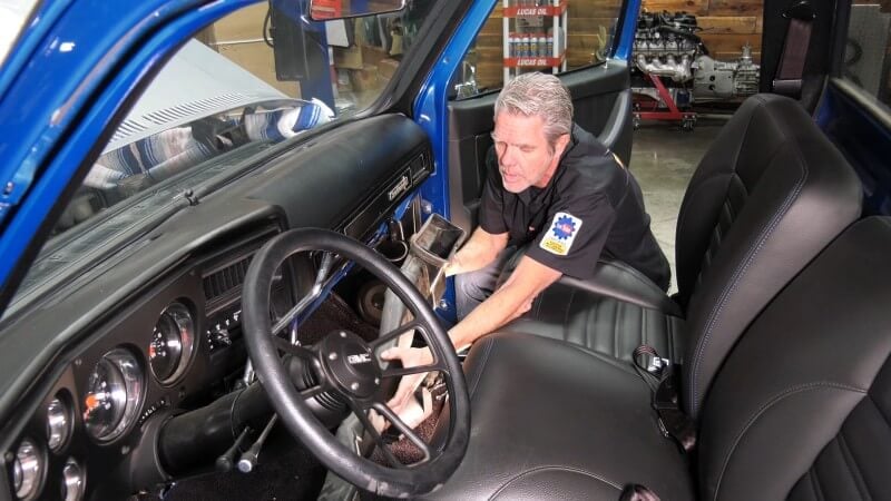 A mechanic sitting in the cab of a classic Chevy truck slotting the A/C components into place underneath the dashboard
