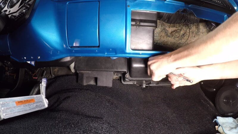 A close up of the underside of the dash in a classic Chevy truck with a mechanic using a socket wrench to remove the heater box fasteners