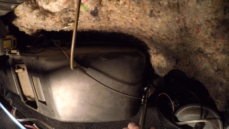 A close up of the underside of the glove box area with a mechanic using a socket wrench and an extension to remove the last heater box mounting bolt