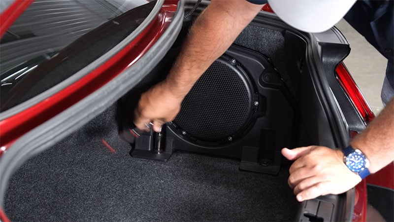 Mechanic removing the lower bolts from an S550 Mustang subwoofer