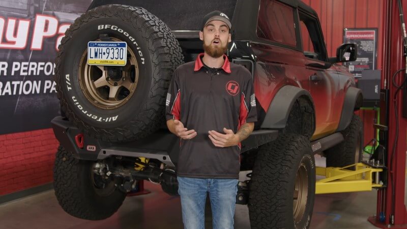 A mechanic standing in front of a Ford Bronco on a hydraulic lift