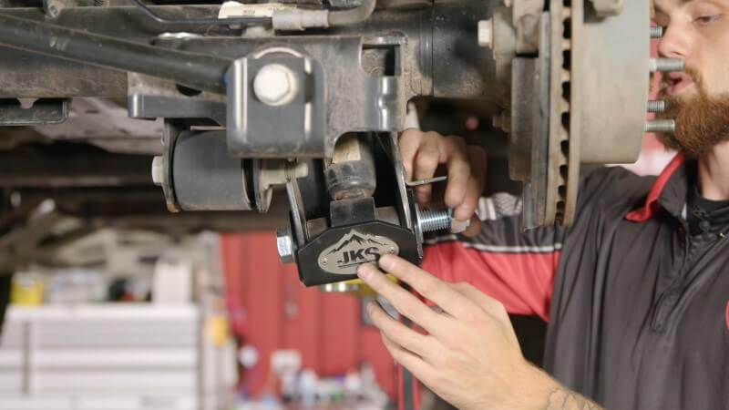 A mechanic screwing a nut onto the end of the strut mounting bolt with his hands