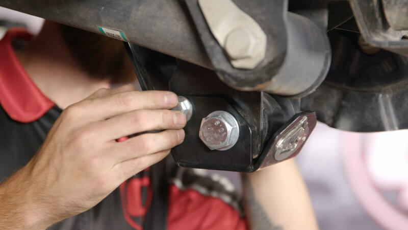 A mechanic hand-tightening the smaller mounting bolt onto the rear shock skid plate