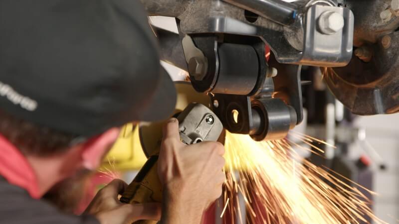 A mechanic cutting off a section of the shock bracket with an angle grinder