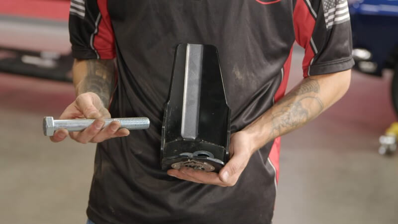 A mechanic holding the rear shock skid plate and washers