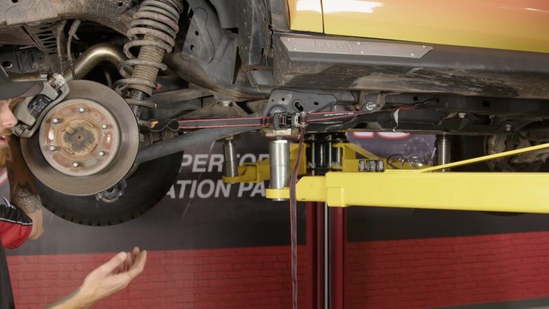 A wide-angle shot of a ratchet strap connecting the rear strut to the frame of a Ford Bronco