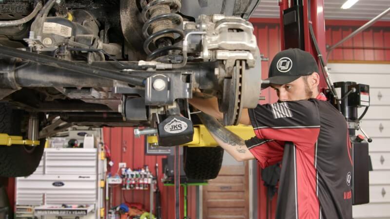 A mechanic loosening the ratchet strap holding the rear strut in place