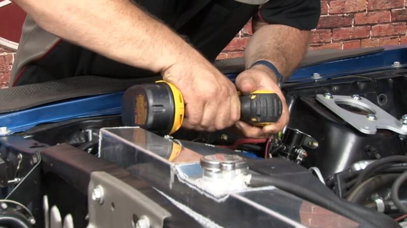 Mechanic driving two holes into the engine bay to mount a bracket