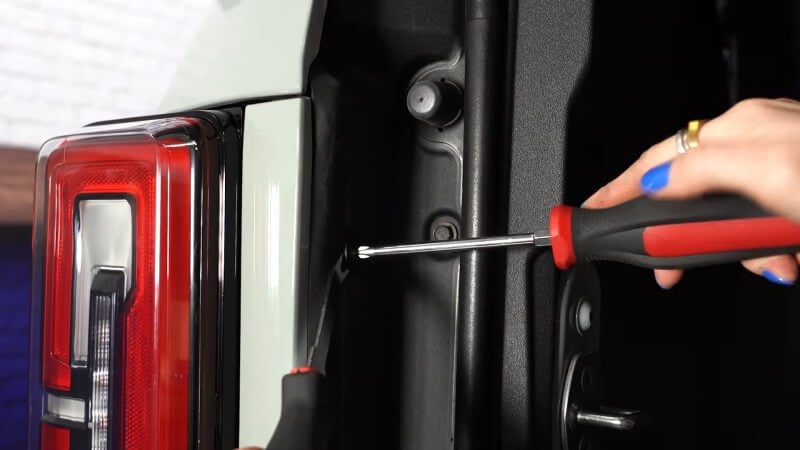 A close up of a mechanic using a screwdriver to loosen an interior panel clip on a white Ford Bronco