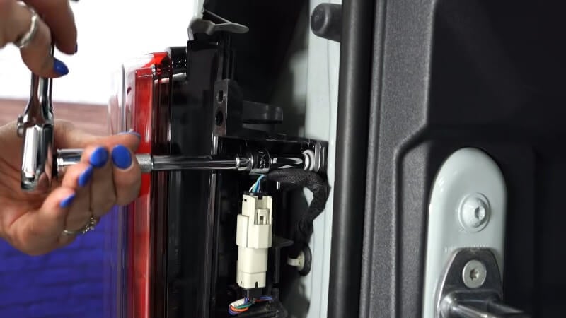 A close up of a mechanic using a ratchet to remove the taillight mounting bolts of a white Ford Bronco