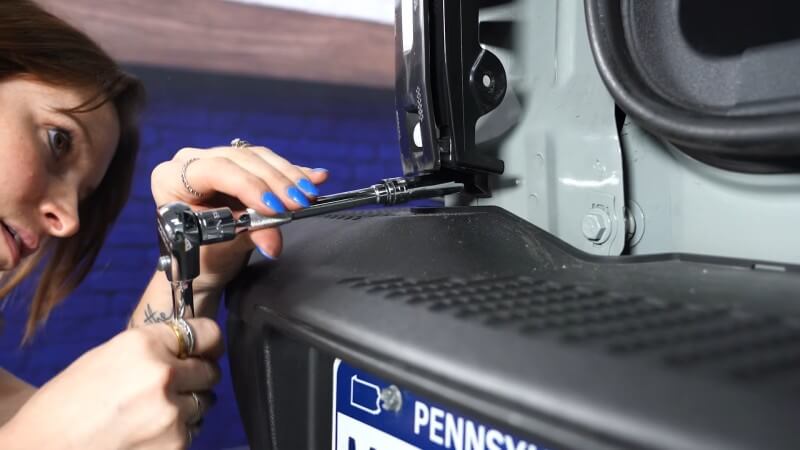 A close up of a mechanic using a ratchet to reinstall the taillight bolts