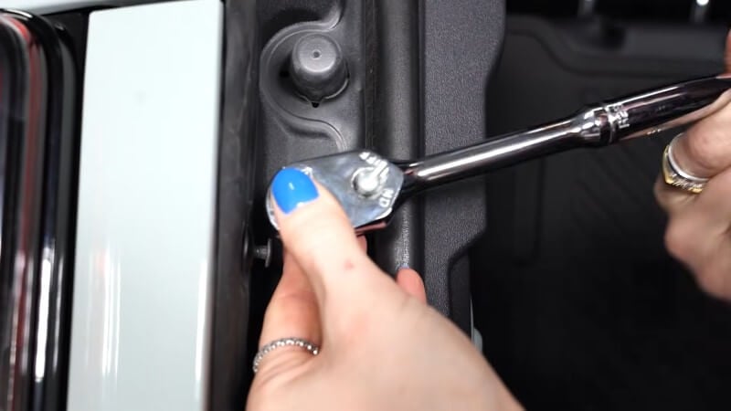 A close up of a mechanic using a ratchet to loosen a trim panel bolt on a white Ford Bronco