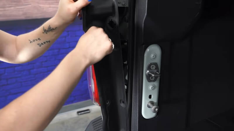 A close up of a mechanic pulling off the interior trim panel of a white Ford Bronco