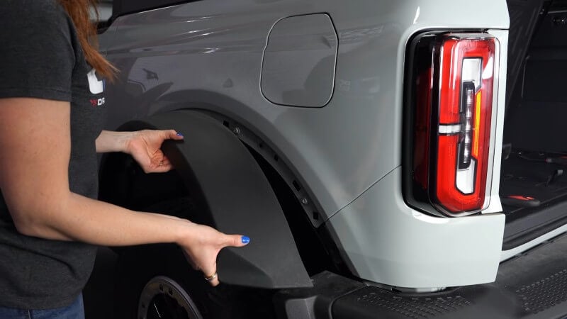 A close up of a mechanic pulling the fender flare of a white Ford Bronco off