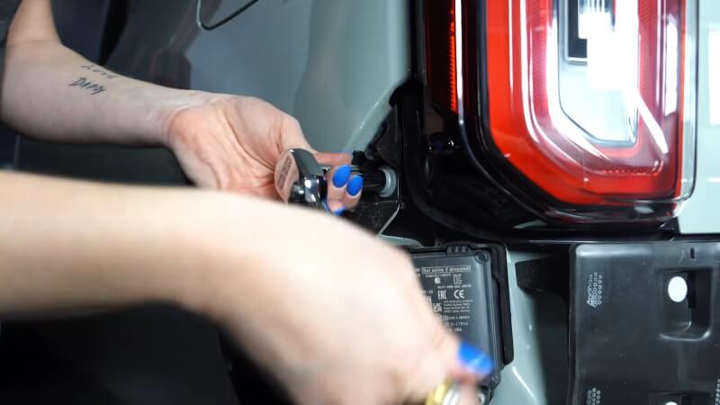 A close up of a mechanic using a ratchet to remove the side taillights bolt of a white Ford Bronco