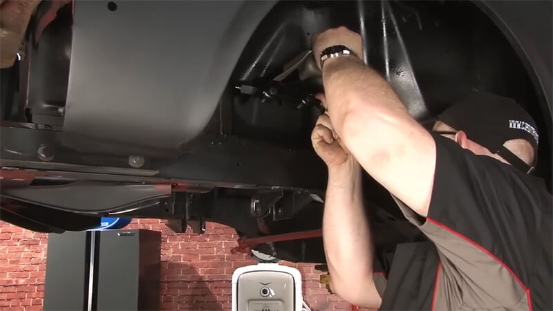 A mechanic reinstalling the rear control arms on a classic Mustang
