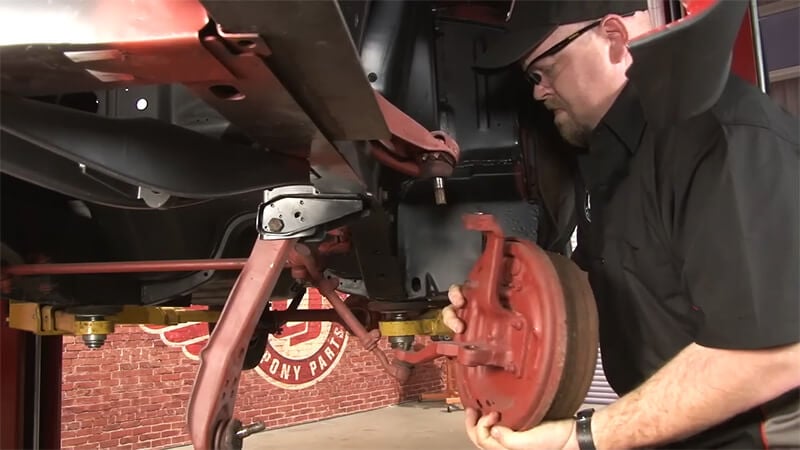 A close up of a mechanic disconnecting the spindle from the upper and lower control arms