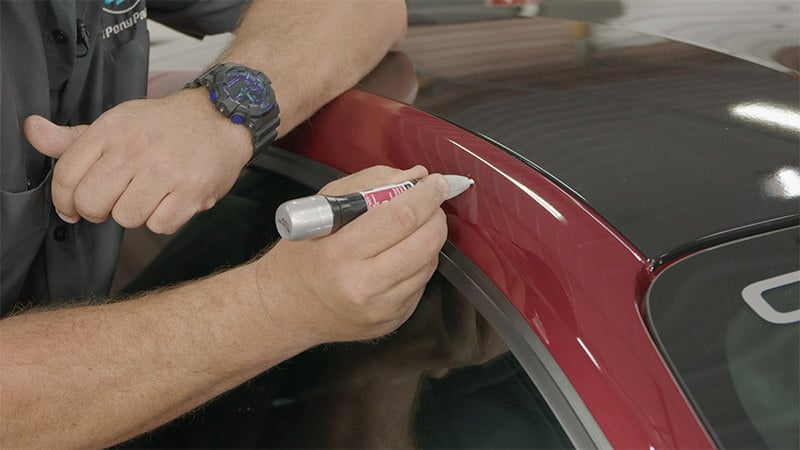 A mechanic using an applicator to carefully apply touch up paint to a red Mustang
