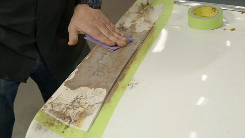 A mechanic sanding a classic Mustang's front fender for paint by hand