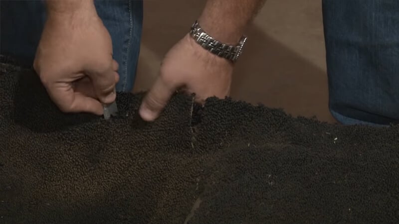Bill uses a razor blade and old carpet to make a cut in the new carpet