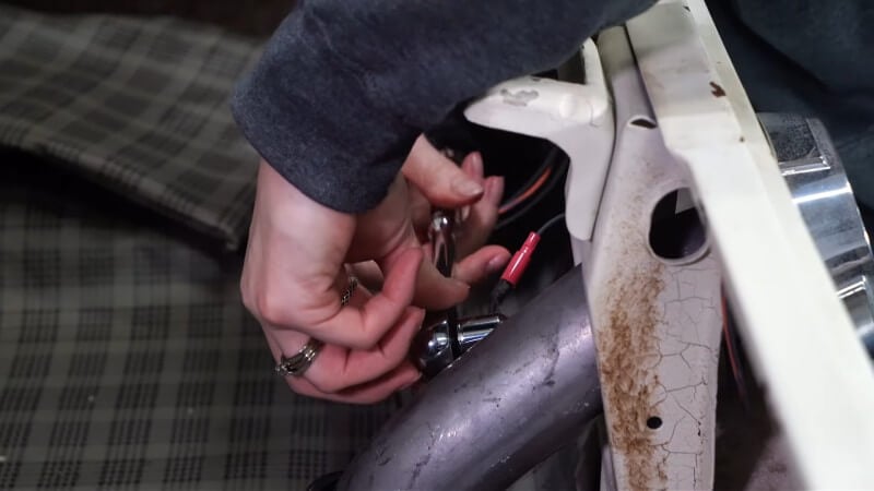 A mechanic using a ratchet with an extension to unscrew the retaining nut of a Ford Mustang's gas cap