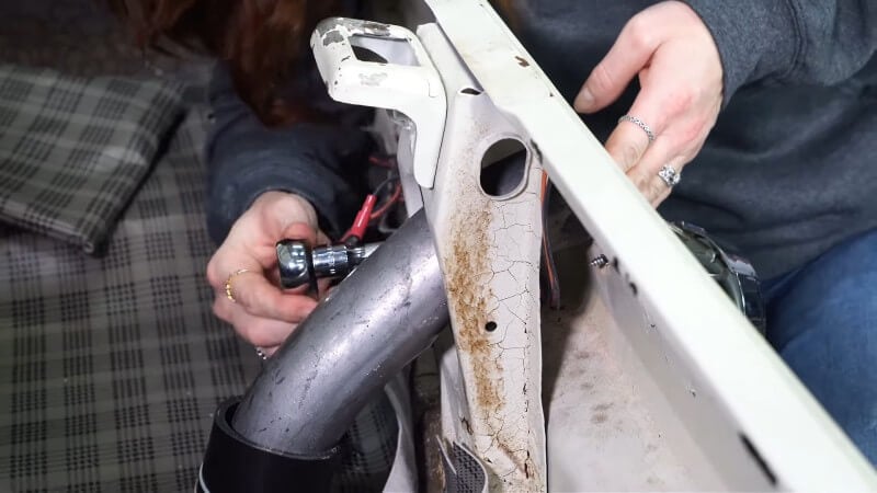 A mechanic using a ratchet with an extension to tighten the retaining nut into place on the inside of the trunk of a classic Ford Mustang