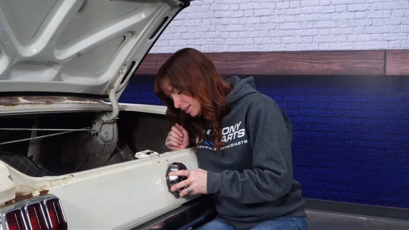A female mechanic screwing the new gas cap into place onto the filler neck of a white classic Ford Mustang