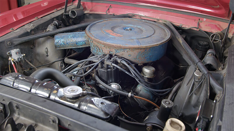 A wide angle shot of an unrestored classic Mustang engine bay