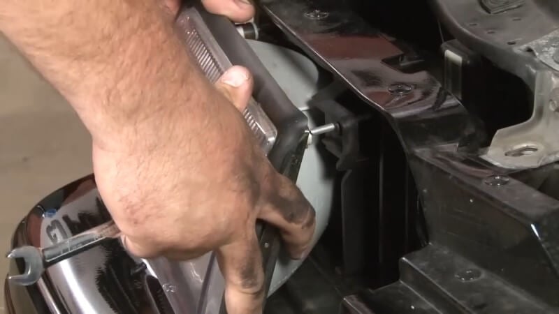 A mechanic removing the headlight of a Fox Body Mustang with his hands
